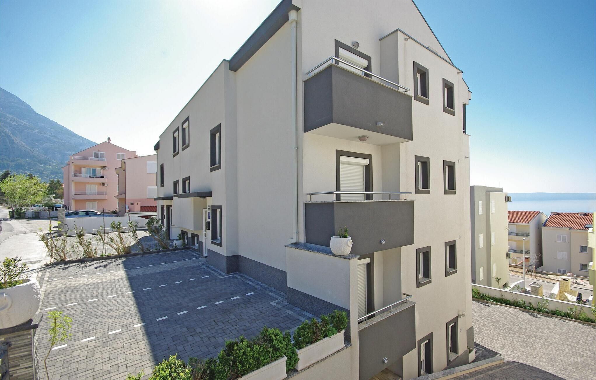 Un immeuble résidentiel moderne à plusieurs étages, doté de balcons, d’une cour pavée et offrant une vue sur les montagnes.