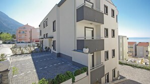 A modern multi-story residential building with balconies, a paved courtyard, and a mountain backdrop. - 1 bedroom nice apartment in Makarska (Makarska)