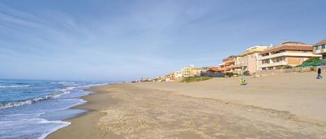 A beach with a clear sky, sandy shore, and buildings along the coastline.