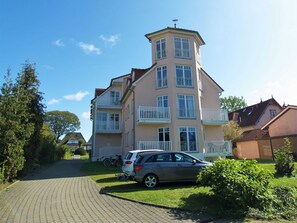 Monikerroksinen rakennus, jossa on parvekkeita, asfaltoitu ajotie ja pysäköity auto.