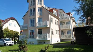 A multi-story building with balconies, a car parked in front, and a grassy area. - Amber Whg. BE-10 .. - Amber Whg. 10 (Kühlungsborn)