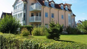 Un hotel de varios pisos con balcones, un jardín y un cielo despejado.