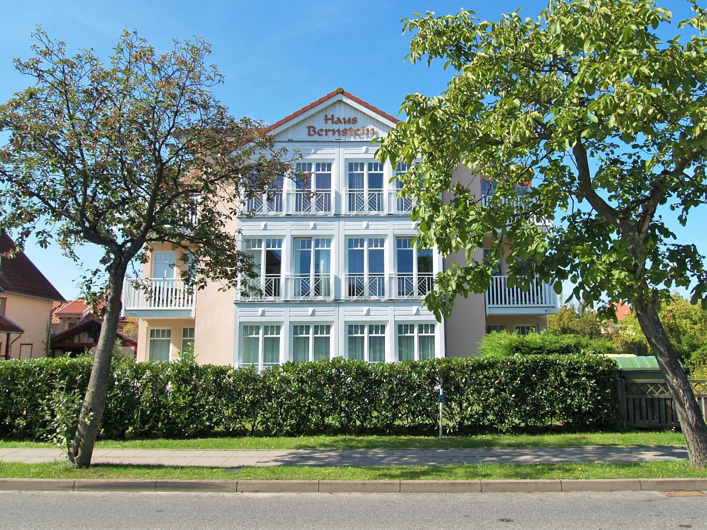 Ein zweigeschossiges Hotel mit der Aufschrift "Haus Bernstein". Es besitzt einen Balkon im zweiten Stock und einen gepflegten Heckenstreifen in der Vorderseite.