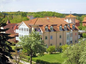 Un immeuble à plusieurs étages, de style architectural européen traditionnel, avec un toit recouvert de tuiles rouges et une combinaison de balcons et de fenêtres.
