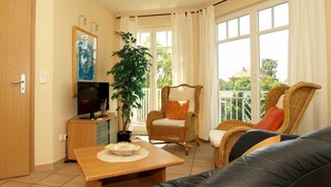 Una sala de estar con televisión, una mesa de comedor con un frutero, una silla y un sofá.