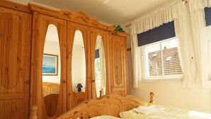 Un dormitorio con una cama de madera, dos camas individuales, un armario grande y una ventana con cortinas.