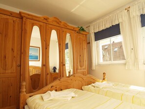 Un dormitorio con una cama de madera, dos camas individuales, un armario grande y una ventana con cortinas.