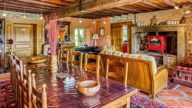 A rustic interior with a wooden dining table, chairs, a sofa, and a red stove.
