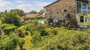 A stone house with a swimming pool, surrounded by lush greenery and potted plants.