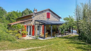 A stone house with a glass conservatory, surrounded by greenery.