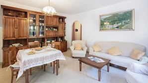 Uma sala de estar com uma mesa de jantar, cadeiras, um sofá, uma mesa de centro e armários de madeira com portas de vidro.