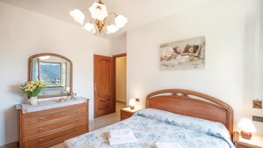 Um quarto com uma cama de madeira, cômoda com espelho, lustre e um quadro na parede.