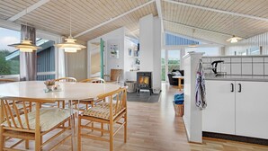 Ein großzügiger Wohnbereich mit hoher Decke, einem Esstisch mit Stühlen, einem Kamin und einer Küchenzeile.