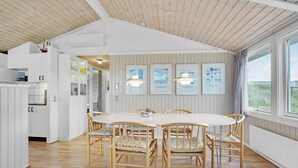Eine moderne Küche mit weißen Schränken, ein Essbereich mit rundem Tisch und Korbstühlen, sowie gerahmte Kunstwerke an der Wand.