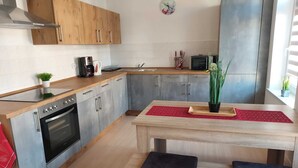 A modern kitchen with wooden cabinets, a stainless steel oven, a built-in microwave, and a red placemat on the table. - Vacation apartments in Chemnitz - Holiday apartment 1 Red (Chemnitz)
