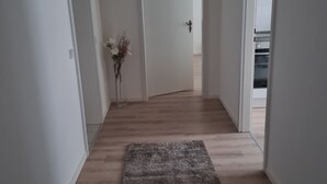 A hallway with a wooden floor, white walls, and a door leading to a kitchen area. - Vacation apartments in Chemnitz - Holiday apartment 1 Red (Chemnitz)