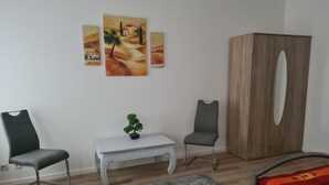 A room with a bed, two chairs, a small table with a plant, a grey rug, and a wooden wardrobe. - Vacation apartments in Chemnitz - Holiday apartment 1 Red (Chemnitz)