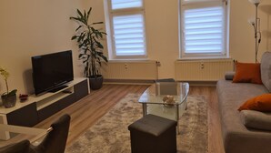 A living room with a flat-screen TV, a glass coffee table, a sofa, and a potted plant. - Vacation apartments in Chemnitz - Holiday apartment 1 Red (Chemnitz)