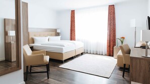 Hotellihuone, jossa on sänky, kaksi tuolia, työpöytä, peili ja ikkuna, jossa on verhot.