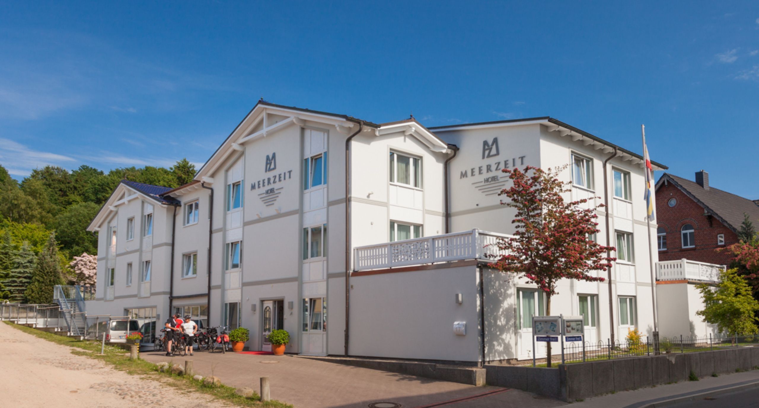 Un hôtel à la façade blanche, doté de nombreuses fenêtres et d’une enseigne indiquant « MEERZEIT HOTEL ».