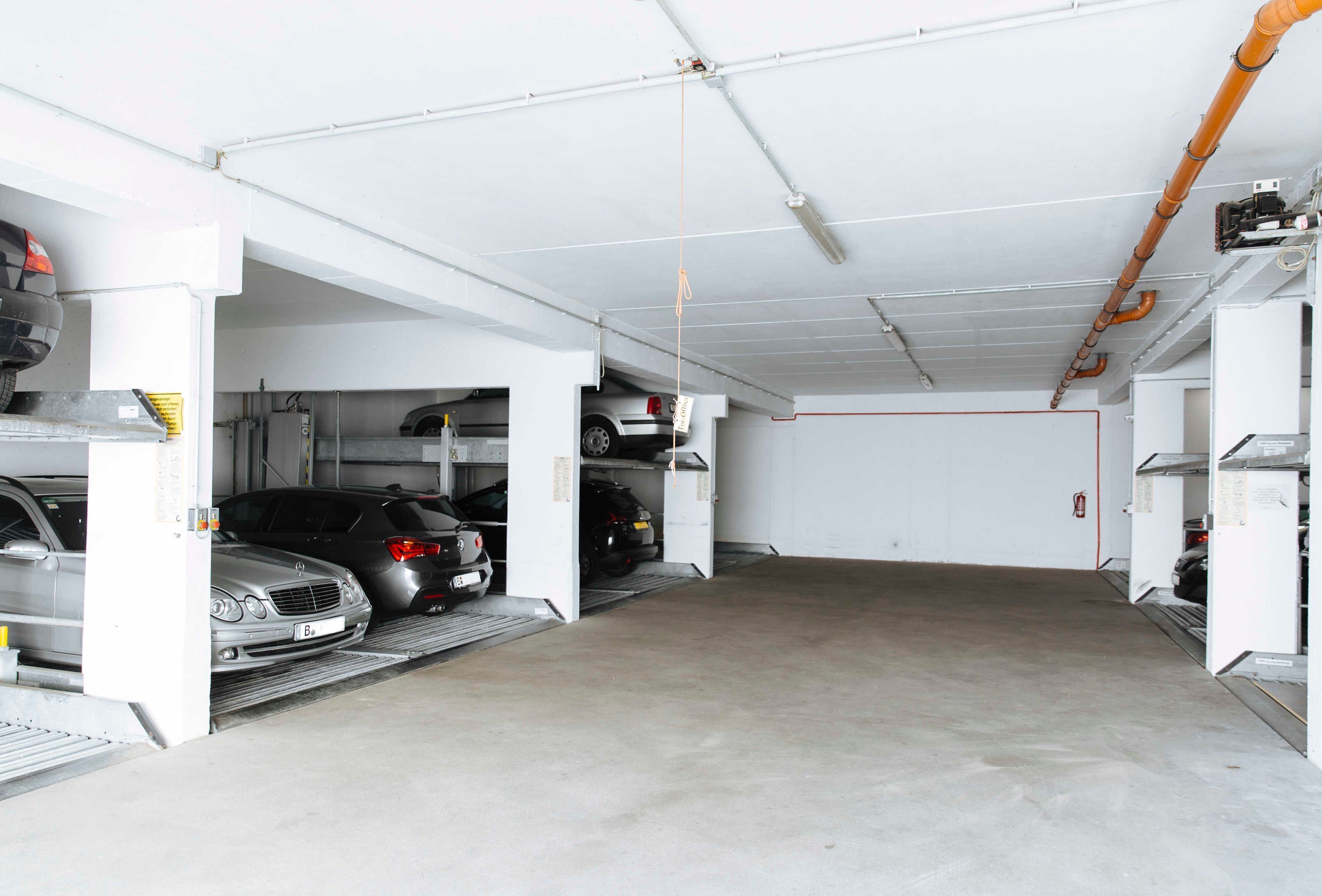Een parkeergarage met meerdere auto's geparkeerd op aangewezen plekken, betonnen vloeren en leidingen aan het plafond.