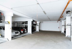Un garaje de estacionamiento con varios coches aparcados en sus espacios designados, pisos de concreto y tuberías en el techo.