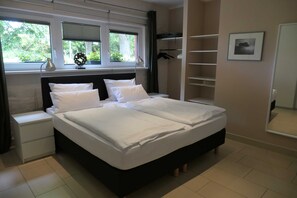 Ein Schlafzimmer mit Bett, Nachttisch, Fenster mit Jalousien, Kleiderschrank und einem gerahmten Bild an der Wand.