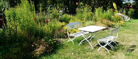 Un jardin avec une table et des chaises en métal blanc, entouré de différentes plantes et arbres.