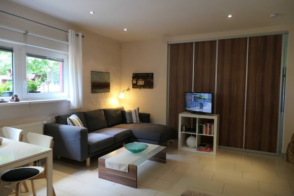 A modern living room with a sofa, coffee table, TV, bookshelf, and a window with curtains. - Feuerstein - Kunsthof Salsitz (Lohme auf Rügen)