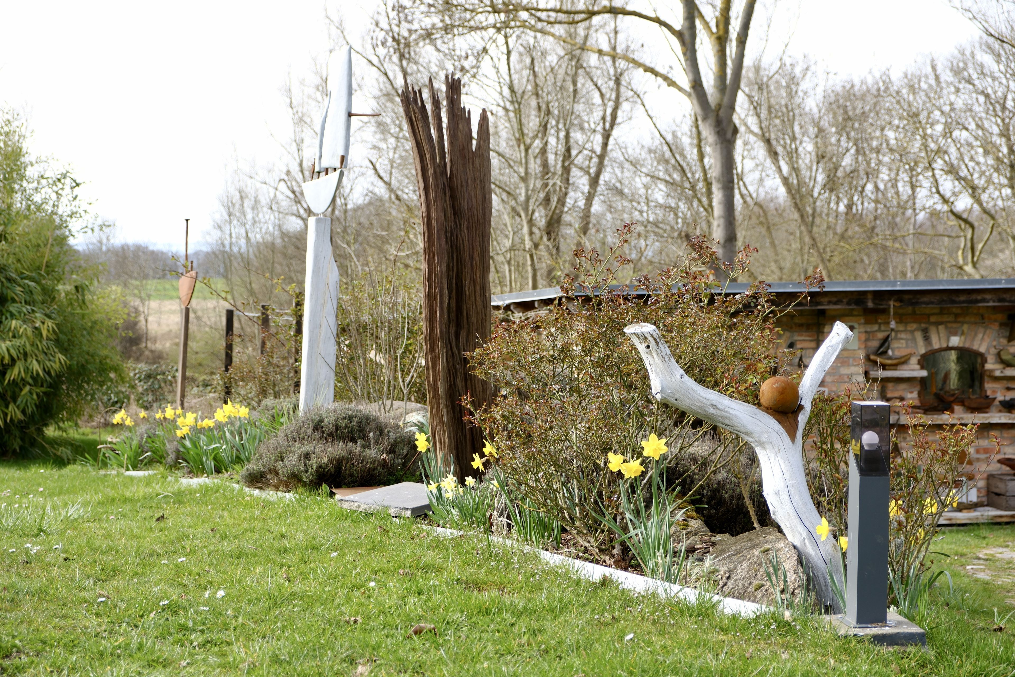 A garden with a white sculpture, a wooden structure, and yellow flowers.