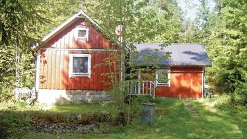 Une cabane en bois rouge, dotée d’un petit porche et d’un toit en métal, entourée d’une végétation luxuriante.