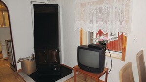 Een woonkamer met een televisie op een houten standaard, een open haard en een kantelaar voor het raam.