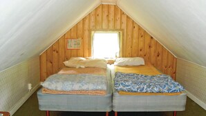 Een kleine zolderkamer met twee bedden, houten wanden, een raam en een zichtbare kalender.