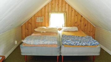 Une petite chambre mansardée avec deux lits, des murs en bois, une fenêtre et un calendrier bien visible.