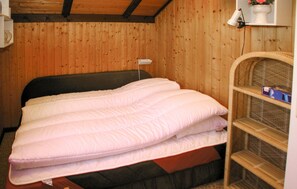 A wooden-paneled room with a bed, a shelf with a lamp, and a wicker chair. - Cozy home in Rømø with house a panoramic view (Rømø)