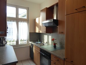 Een keuken met houten keukenkastjes, een fornuis, een spoelbak en een raam met gordijnen.