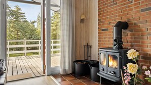A room with a wood-burning stove, a sliding glass door to a deck, and a brick wall. - Amazing home in Aakirkeby with kitchen (Aakirkeby)