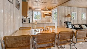 A spacious dining area with a large wooden table and wicker chairs, a kitchen in the background, and a leather sofa in the living area. - Amazing home in Aakirkeby with kitchen (Aakirkeby)