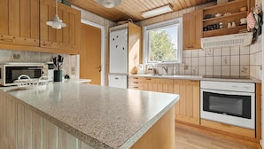 A kitchen with wooden cabinets, a granite countertop, a microwave, a refrigerator, a sink, and a window with a view of greenery. - Amazing home in Aakirkeby with kitchen (Aakirkeby)