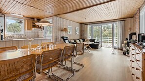 A spacious living area with a wooden ceiling, a dining table with chairs, a sofa, and a kitchen area with a window. - Amazing home in Aakirkeby with kitchen (Aakirkeby)