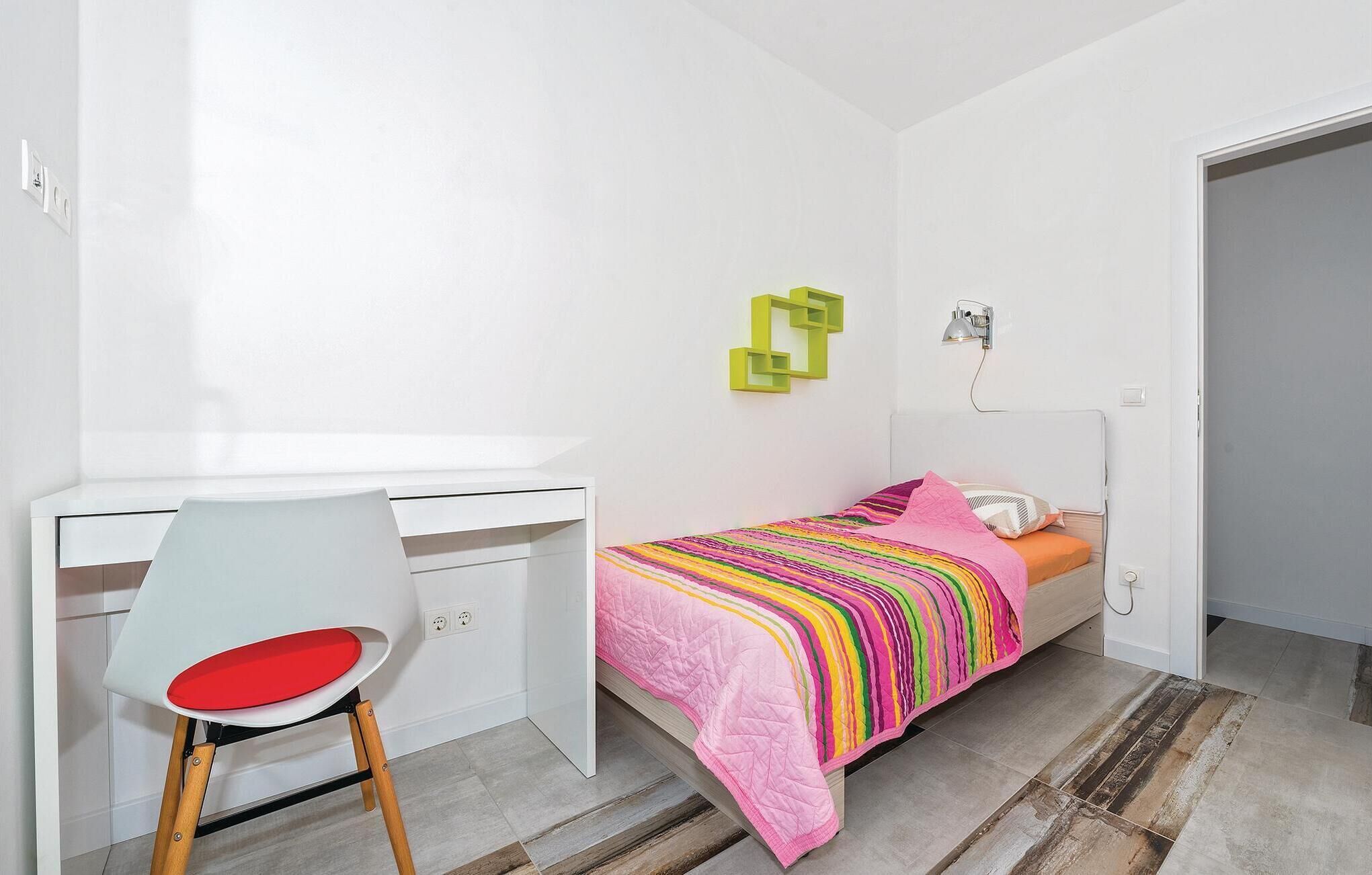 Quarto pequeno e moderno com cama, escrivaninha e cadeira.