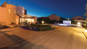 A hotel courtyard at dusk with a swimming pool, outdoor seating, and a boat.