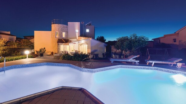 A swimming pool with lounge chairs and a well-lit patio area.