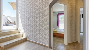 A modern hotel interior with a patterned wall, a staircase leading to a balcony, and a view of the outside.