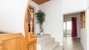 A staircase with wooden railings leading to a room with patterned wallpaper and a potted plant.