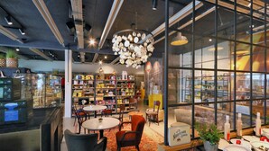 Een gezellige boekwinkel met ronde tafels en stoelen, boekenplanken vol boeken en snuisterijen, en een bijzondere plafondlamp gemaakt van theekopjes.