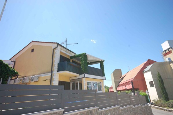 A modern two-story house with a balcony, a visible satellite dish, and a gated entrance.