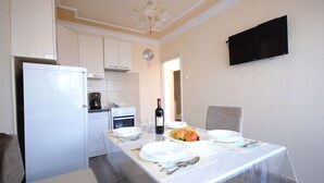 Una cocina compacta con electrodomésticos blancos, una mesa de comedor con platos, una botella de vino y un frutero.