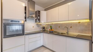 A modern kitchen with white cabinets, a stainless steel oven, a coffee maker, and a fruit bowl on the counter.