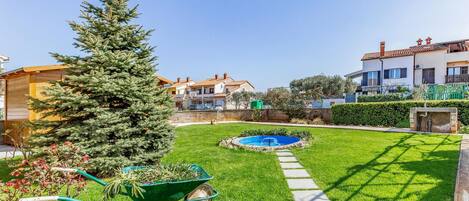 A well-maintained garden with a lawn, a small pool, and a wheelbarrow with plants.